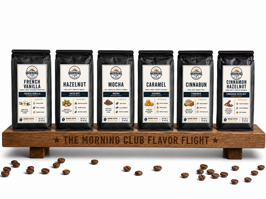 Morning Club Flavor Flight sample pack featuring six flavored coffees including French Vanilla, Hazelnut, Mocha, Caramel, Cinnabun, and Cinnamon Hazelnut on wooden display stand